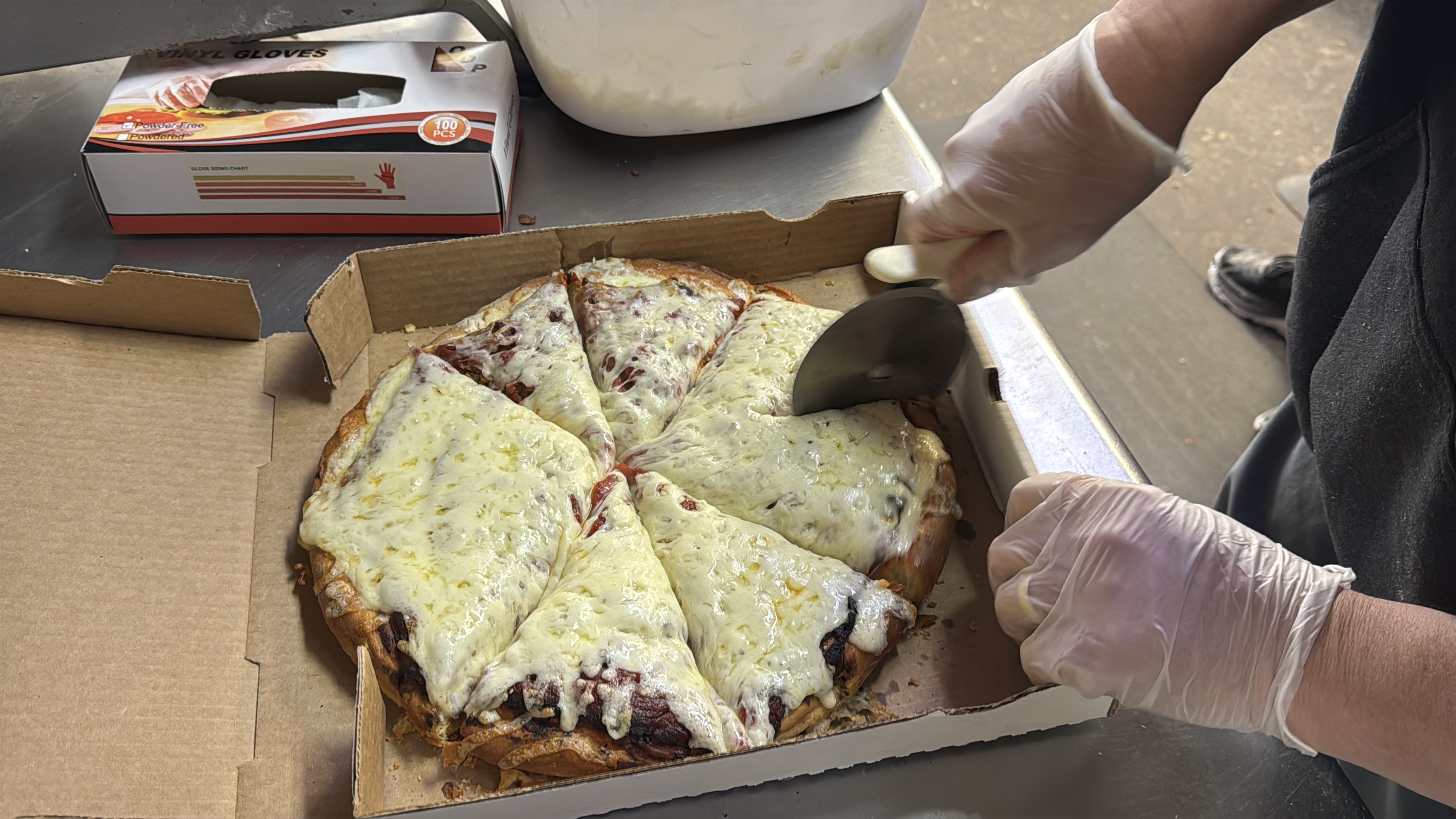 Fresh cheese pizza being sliced in a takeout box